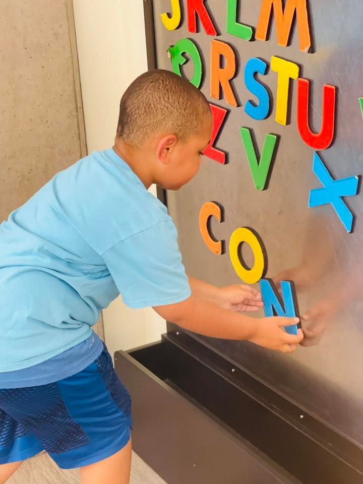 Child placing colorful letters on a wall-mounted board in a classroom.