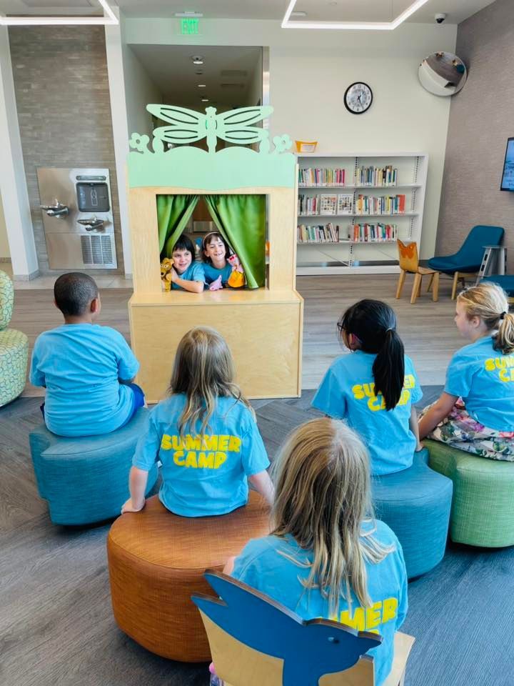 Children sitting in a library story time circle watching a puppet show on a small stage