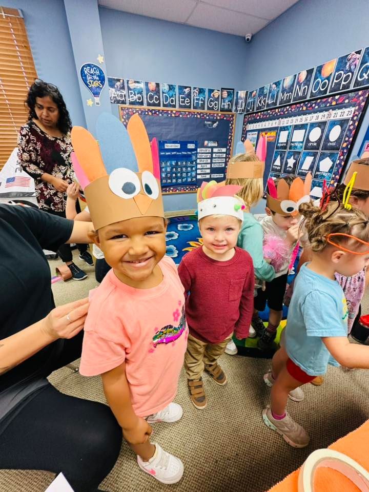 Children in a classroom wearing colorful paper antlers and holiday headbands, smiling and playing