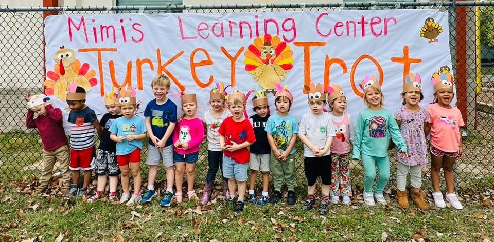 Children posing in front of a “Mimi’s Learning Center Turkey Trot” banner with colorful fall decorations