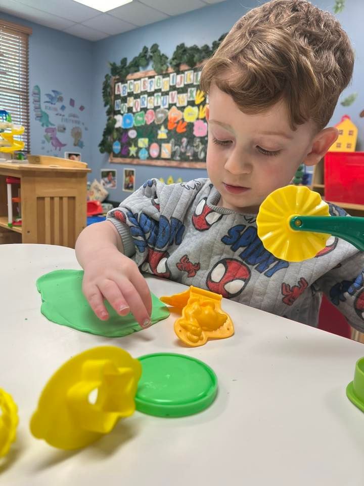 Child molding yellow and green clay at a classroom table with playdough tools