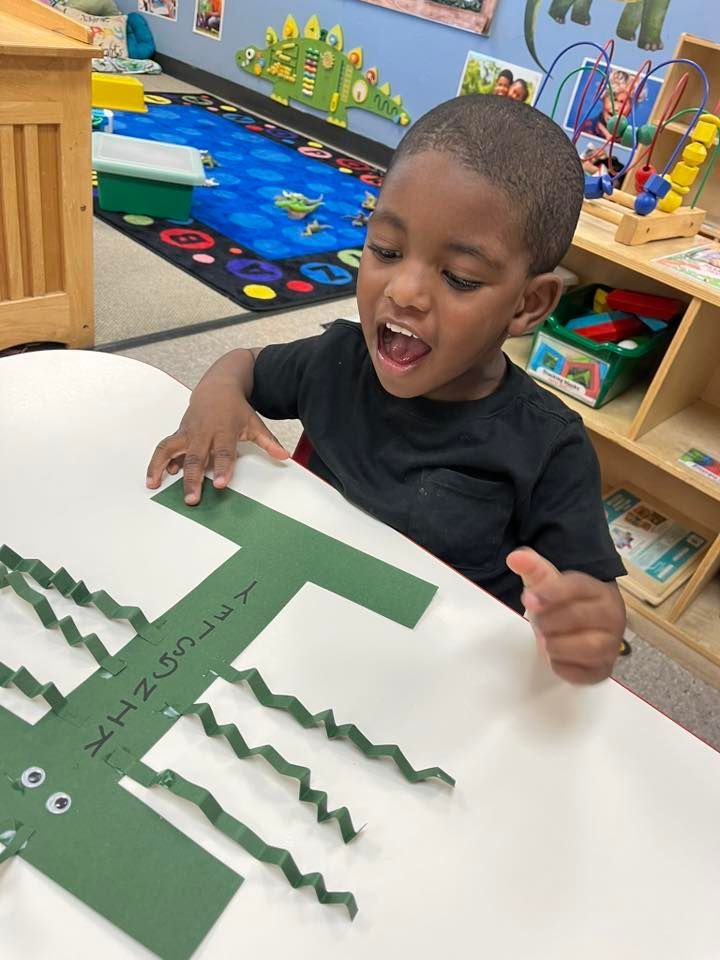 Child at a table arranging green paper strips in a classroom activity.