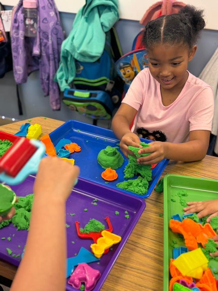 Child playing with colorful molding clay at a table in a classroom setting