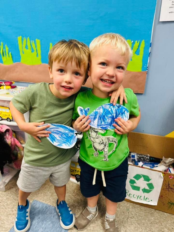 Two children smiling and holding painted paper plates in a classroom or daycare setting