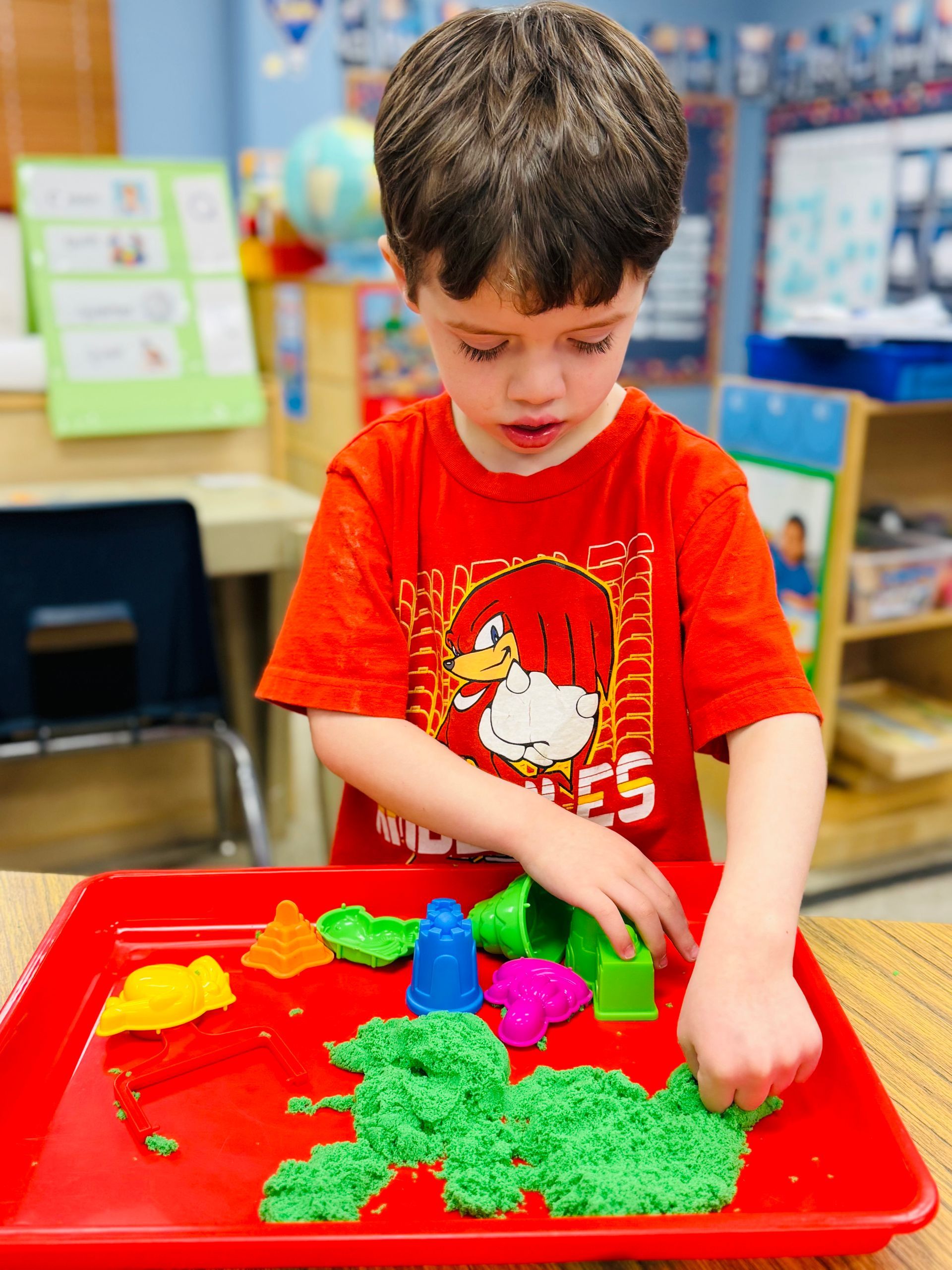 Child playing with colorful modeling clay at a table in a classroom
