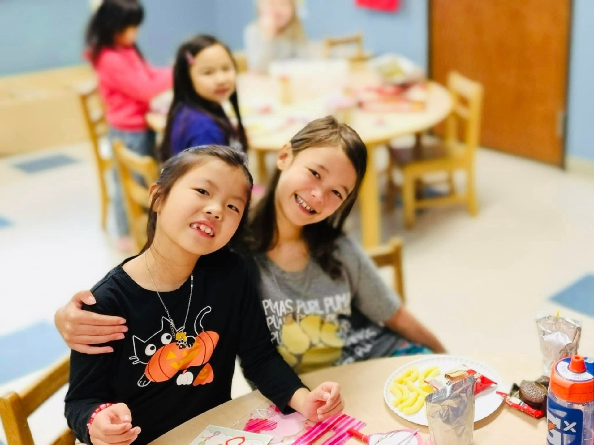 Children smiling at a classroom table with art supplies and snacks