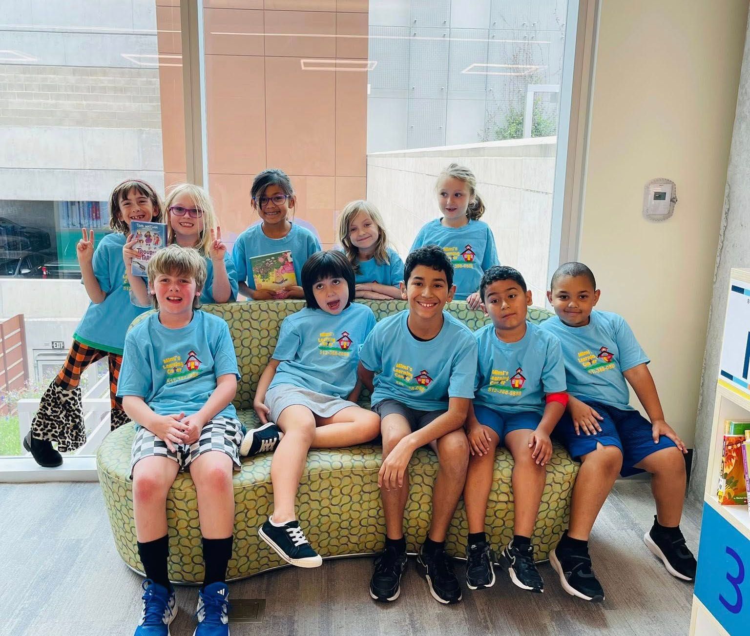 Group of people in matching blue shirts sitting and standing in a bright room, smiling at the camera.