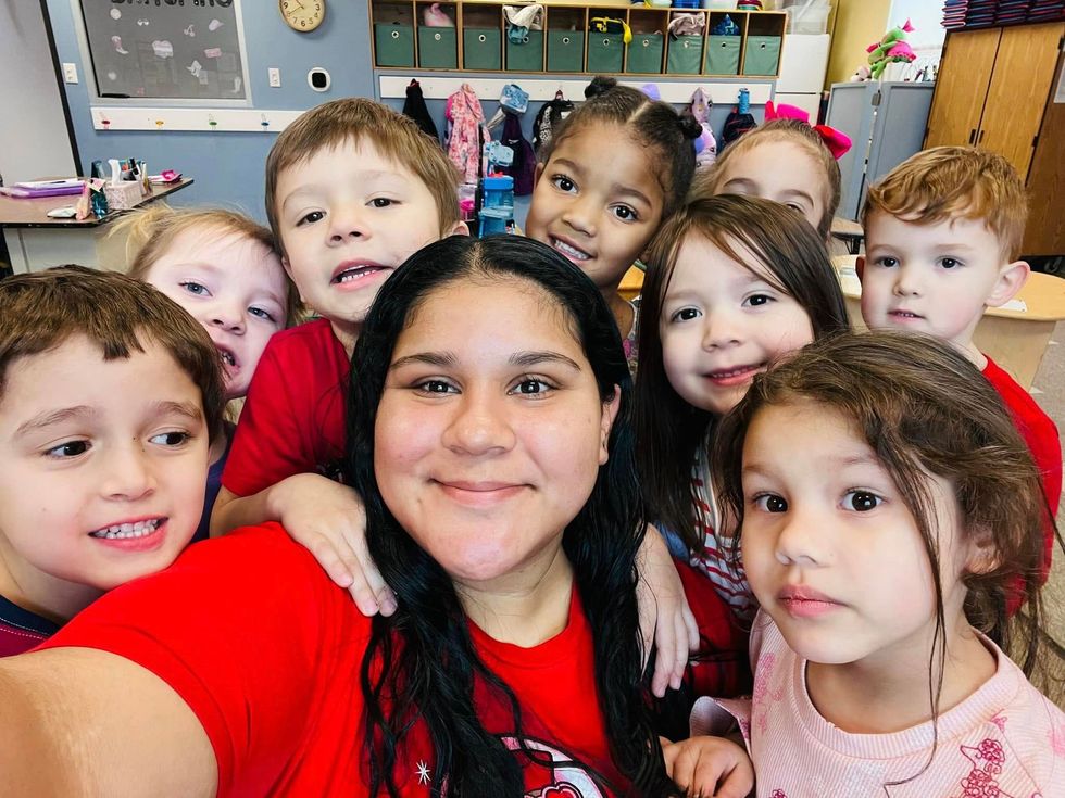 Group selfie in a classroom, with smiling children behind a woman in a red shirt.