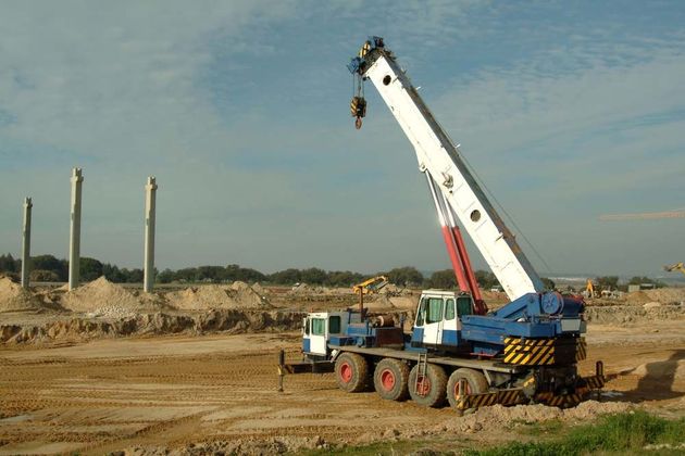 Crane truck lifting a worker at a dusty construction site with concrete pillars in the background