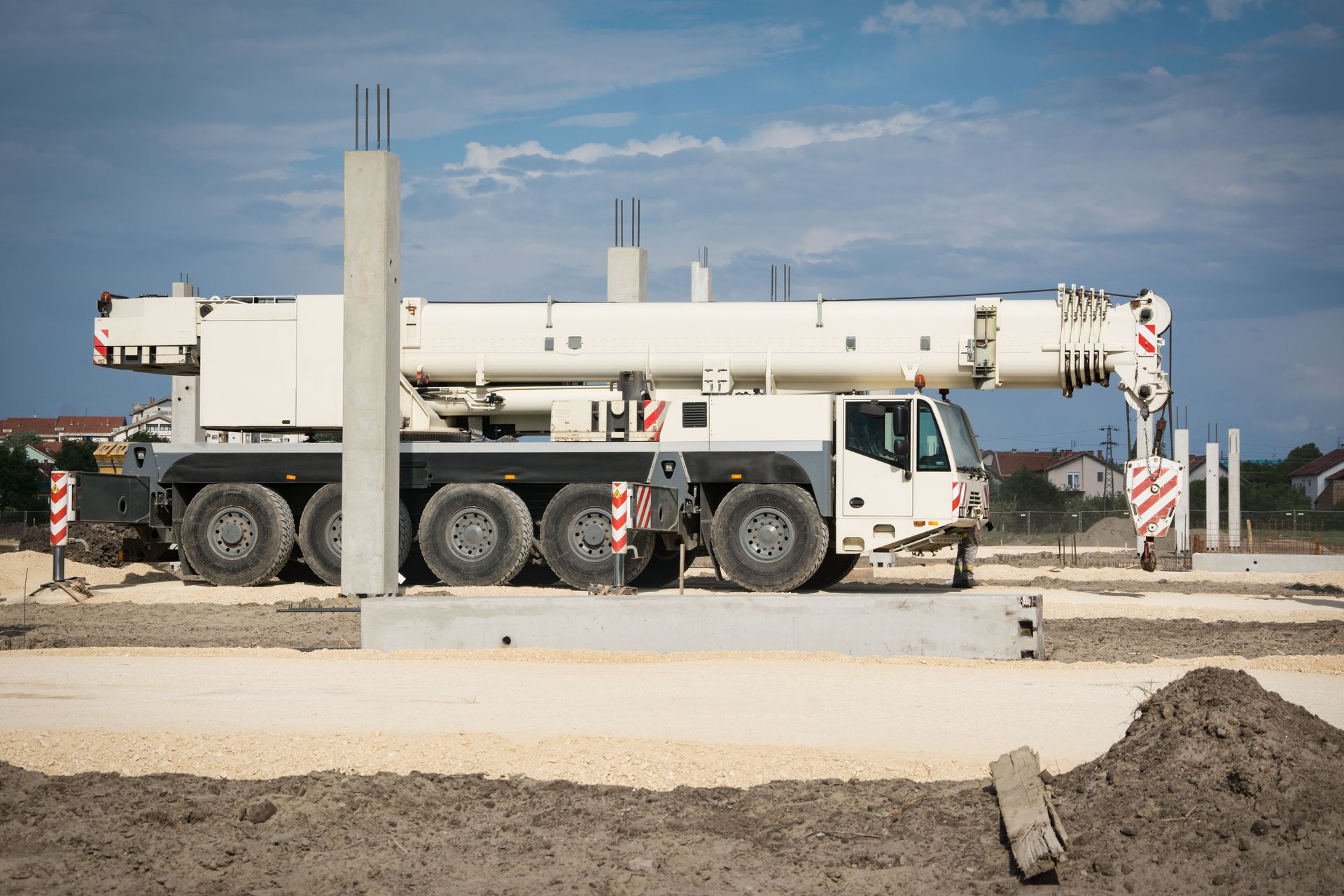 Large white crane truck at a construction site, parked beside a concrete barrier under a blue sky.