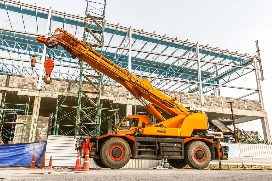 Orange crane truck at a construction site lifting materials beside a steel-frame building