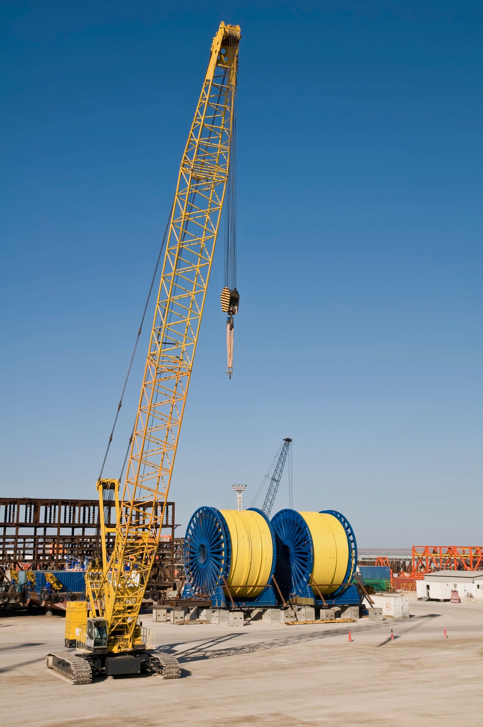 Yellow construction crane lifting cable reels at a site under a clear blue sky