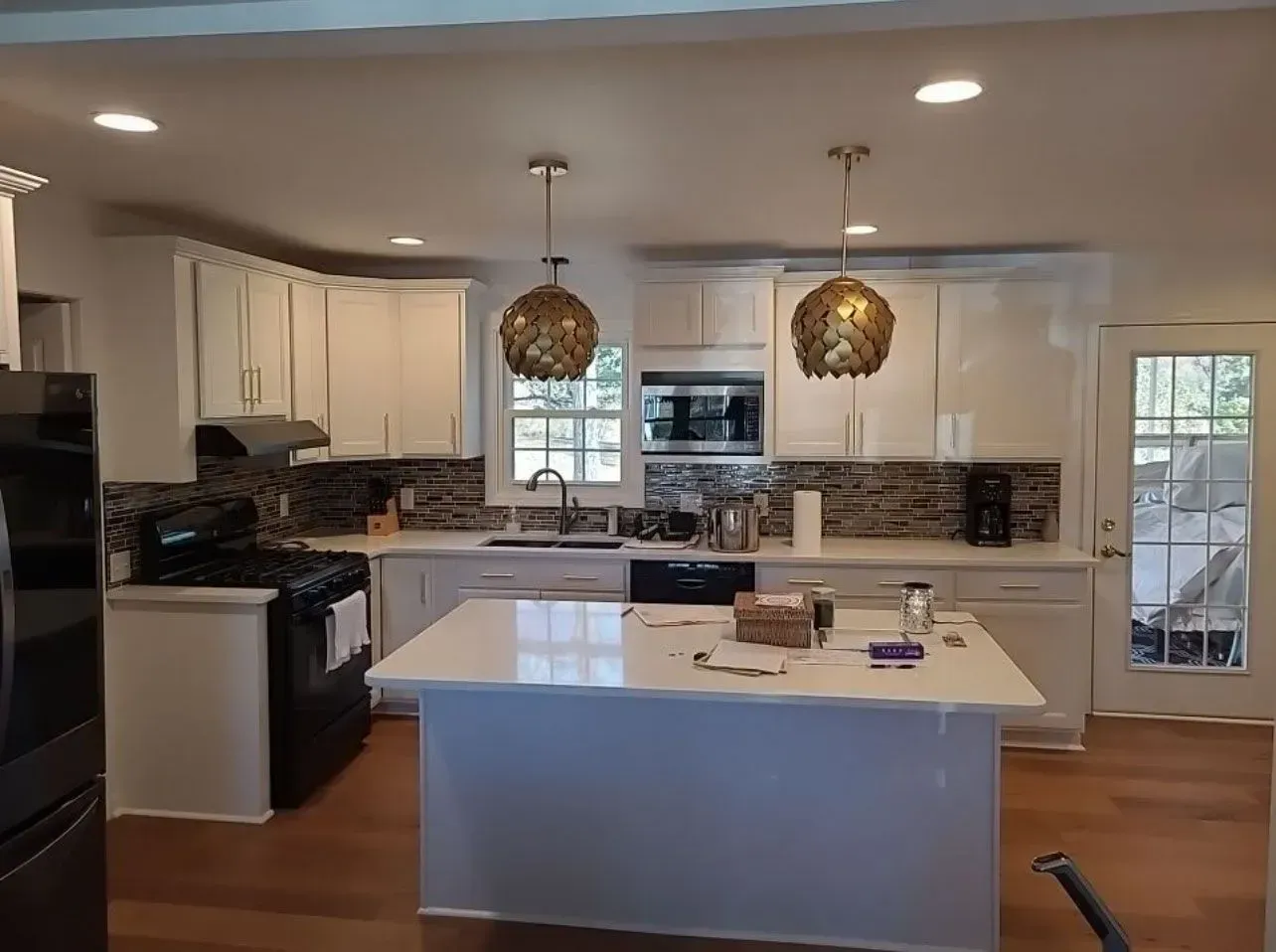 Kitchen with white cabinets, island, and gold pendant lights. Dark appliances and wood floors.