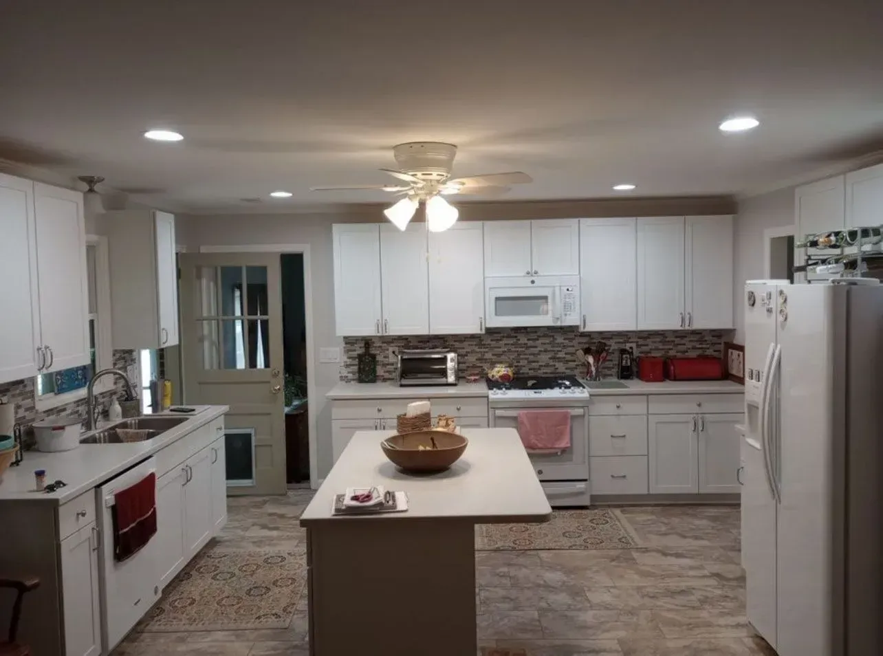 White kitchen with white cabinets, island, and appliances. Stone backsplash.