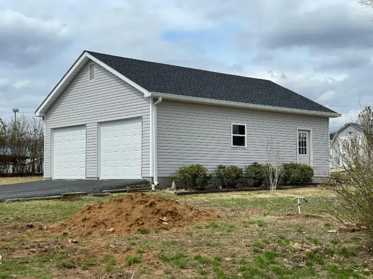 Two-car garage with light gray siding, dark roof, two garage doors, and a side door.
