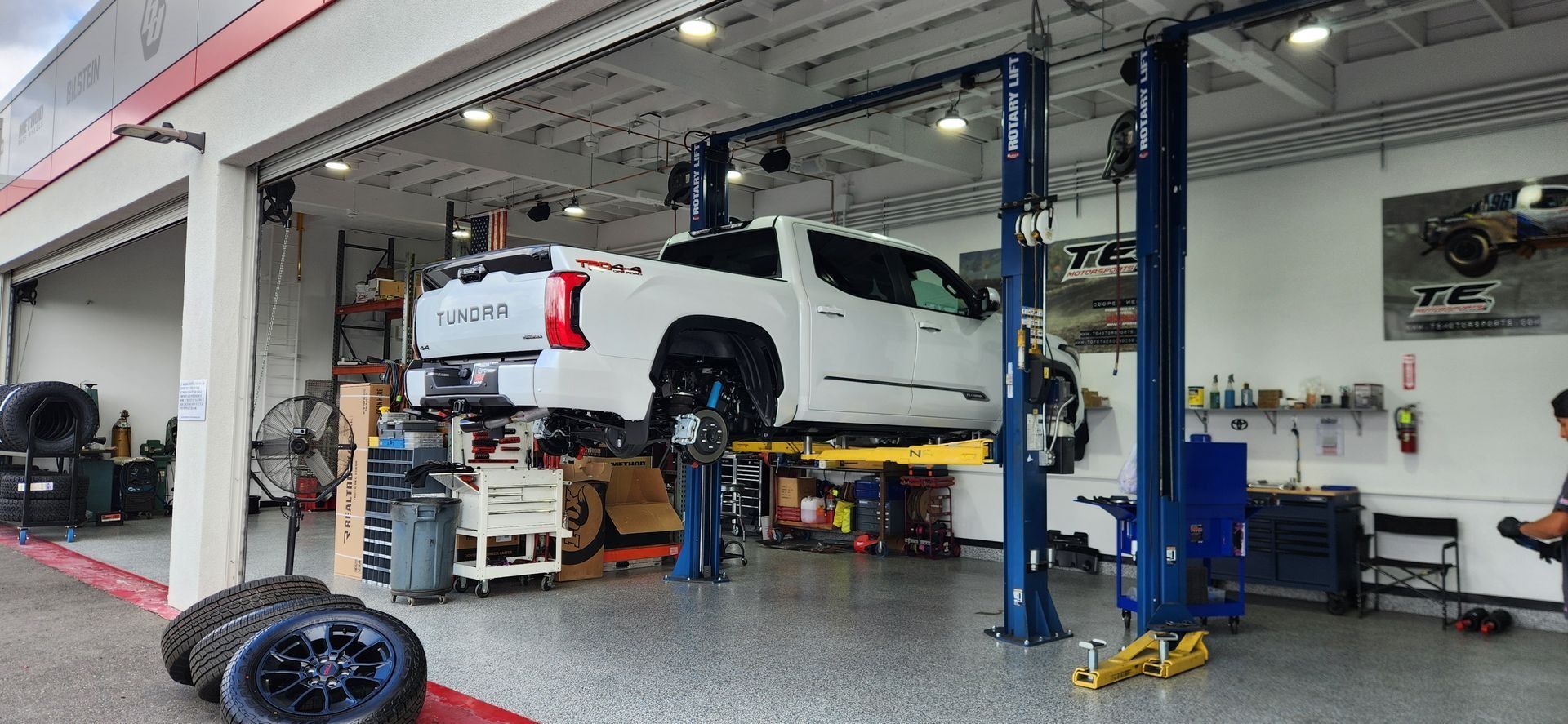 White truck on a lift inside a garage. Other car parts are on the floor.