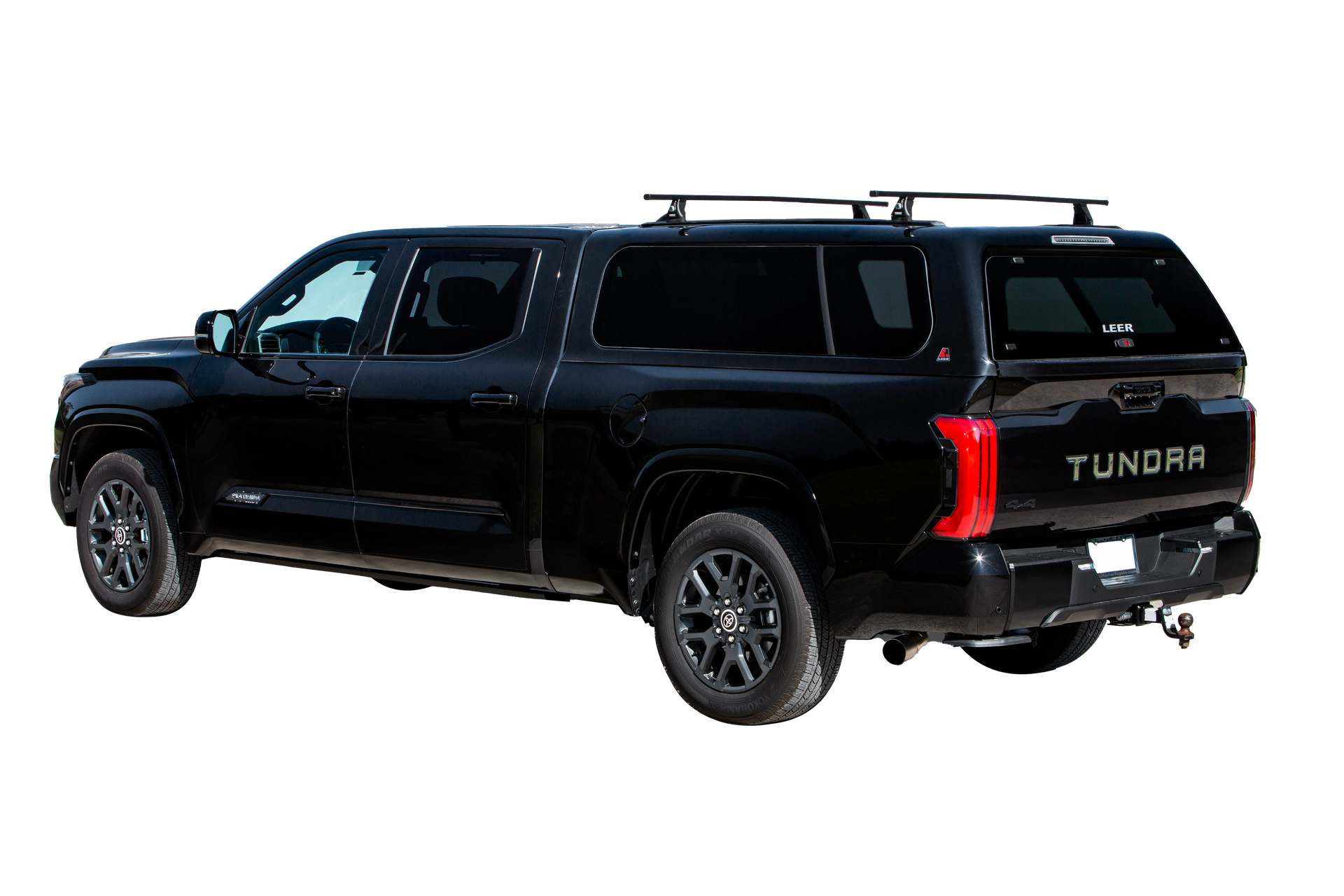 Black pickup truck with a white camper shell driving on a road in a grassy field with sheep.