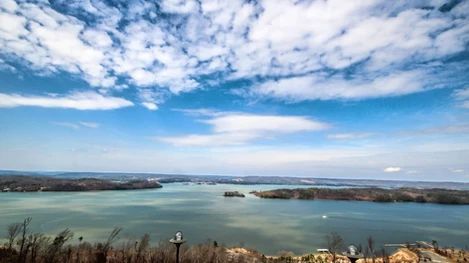 A large body of water surrounded by trees under a cloudy blue sky.