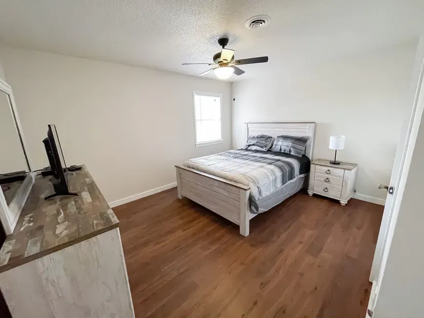 A bedroom with a bed , dresser , nightstand , television and ceiling fan.