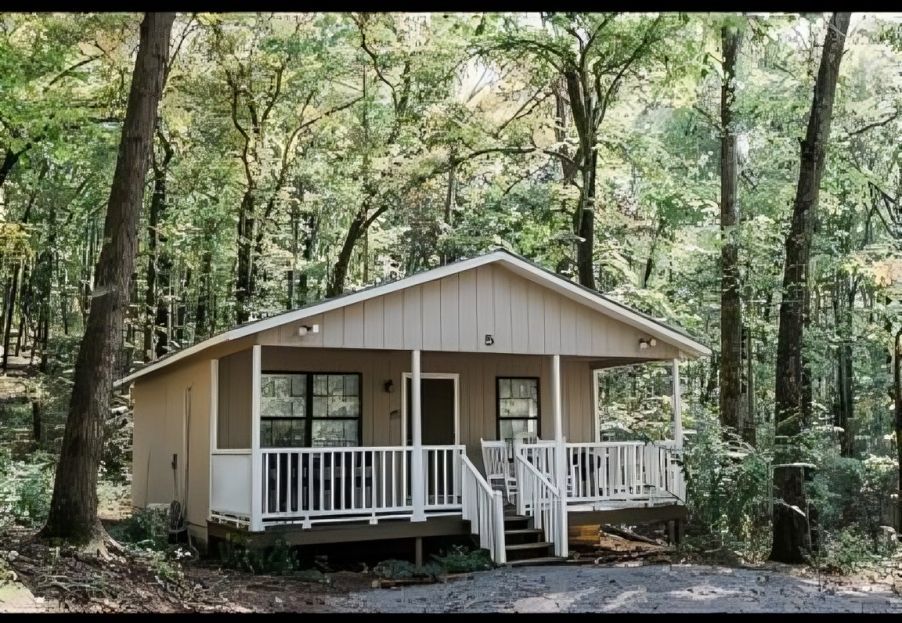 A small house with a porch in the middle of a forest.