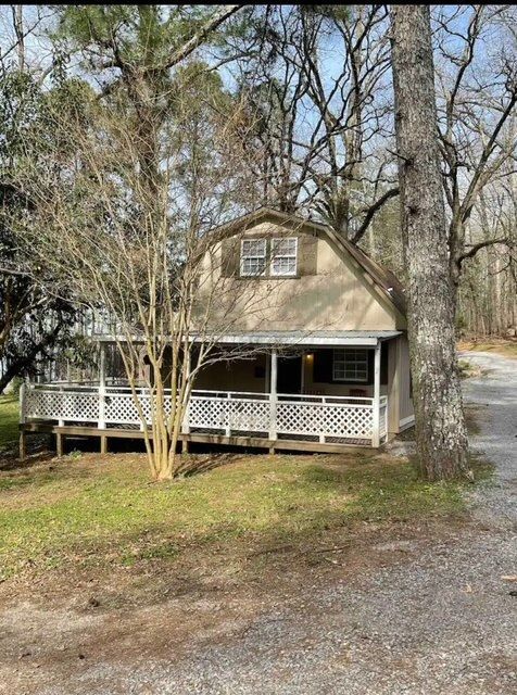 A small house with a porch and trees in the background.