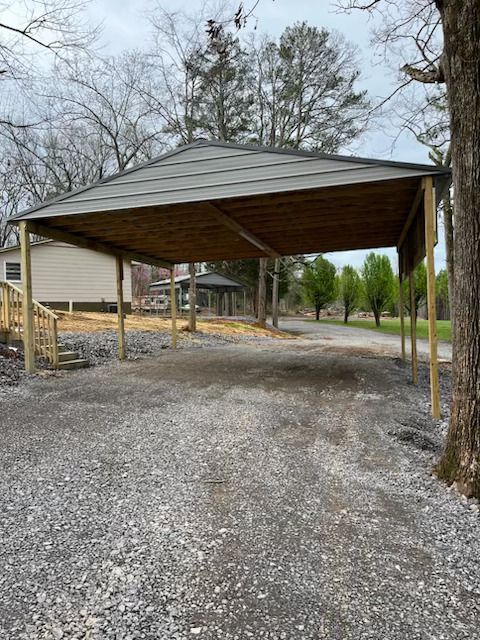 A carport is sitting on the side of a gravel road.