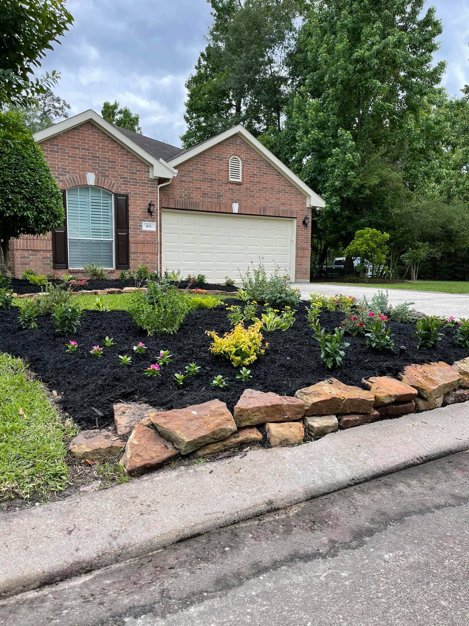 A brick house with a white garage door and a rock garden in front of it