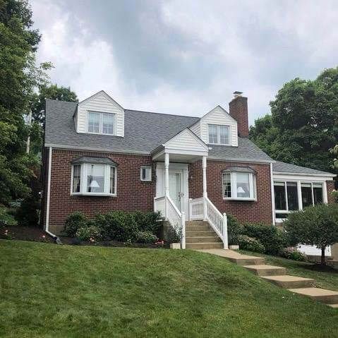 A brick house with a gray roof and white trim is sitting on top of a lush green hill.