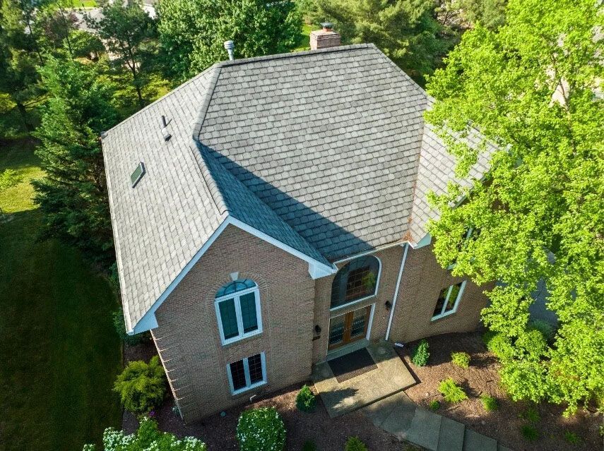 An aerial view of a large brick house with a gray roof surrounded by trees.