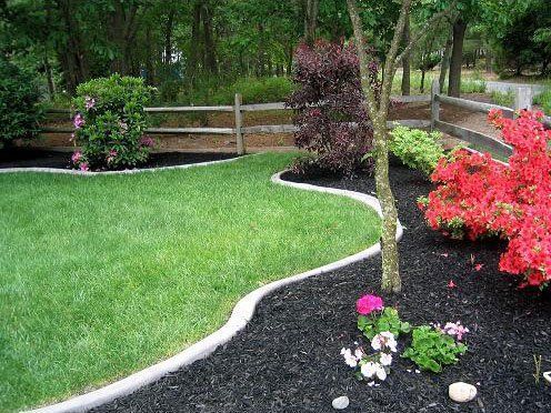 a lush green lawn with a fence in the background and flowers in the foreground