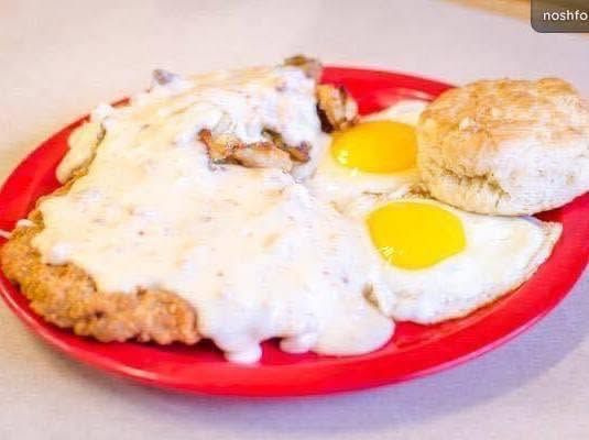 Red plate with fried eggs and smothered breaded cutlets in white gravy on a table