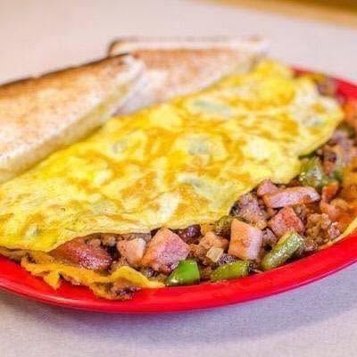 Omelet on a red plate with toast and diced potatoes, topped with melted cheese