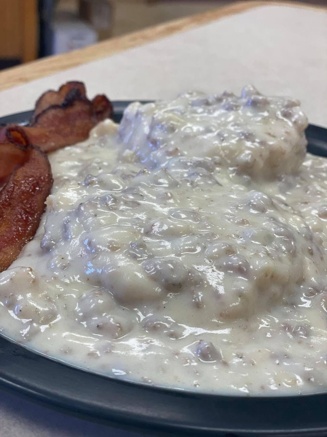 Plate of biscuits and gravy with bacon on a blue-rimmed plate