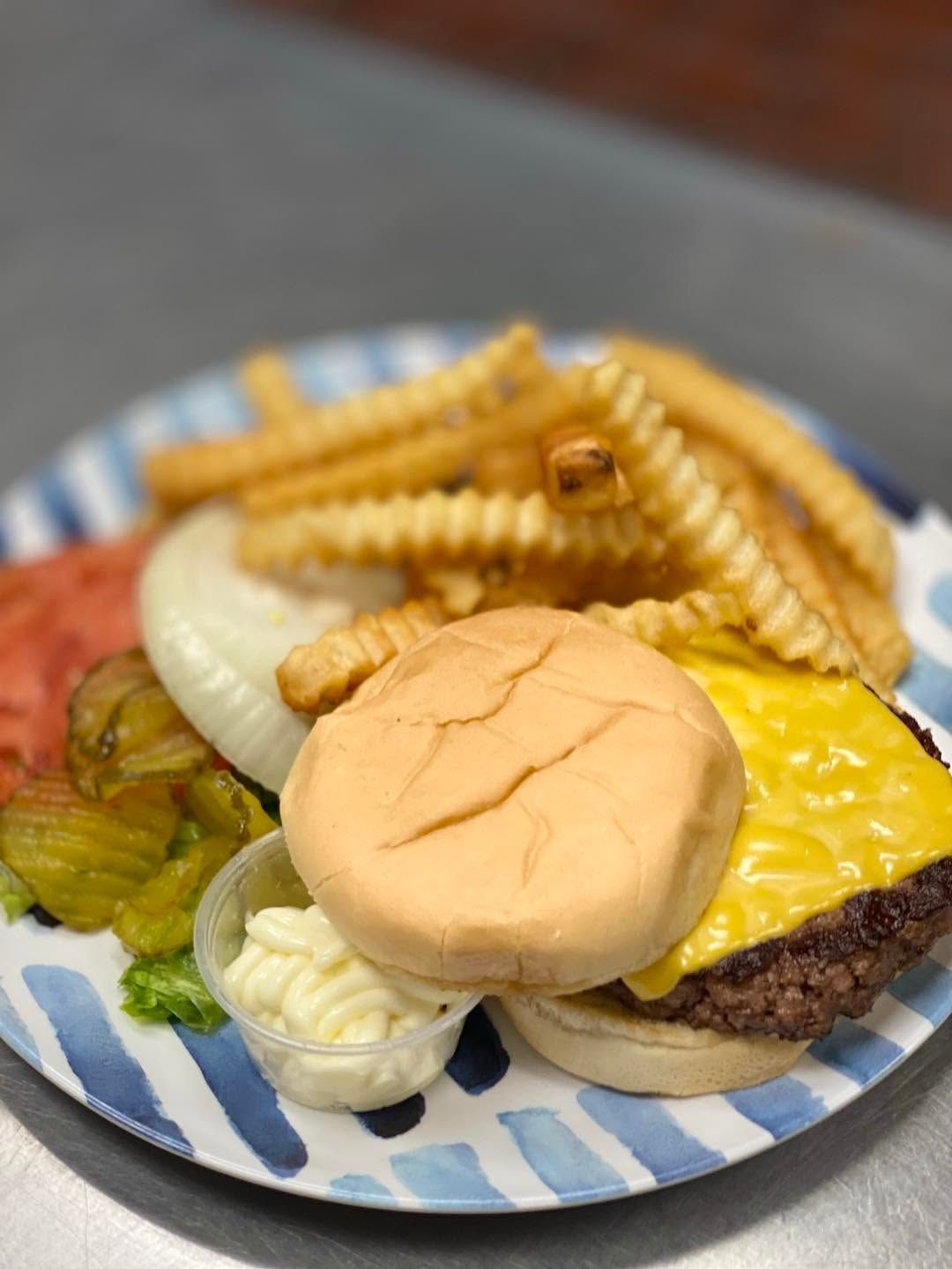 Burger and crinkle-cut fries on a blue-and-white plate with a pickle and onion slices