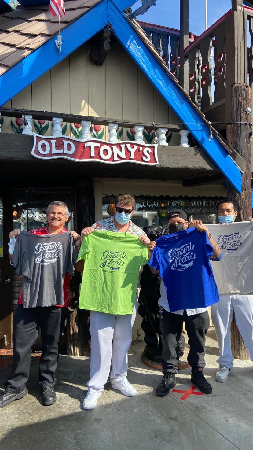 People holding shirts in front of Old Tony's restaurant, with a blue roof and red and white sign.