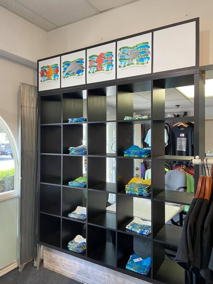 Black shelving unit displaying folded shirts and art in a retail store.