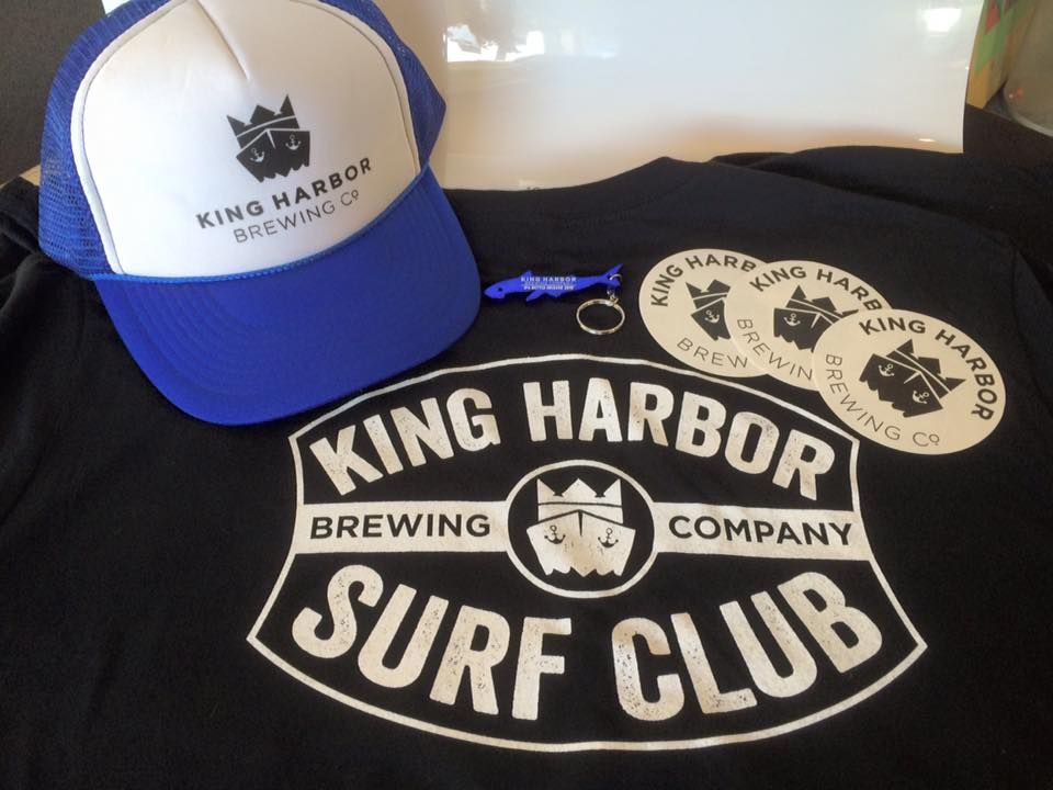 King Harbor Brewing Co. merchandise: hat, t-shirt, stickers, and keychain on a table.