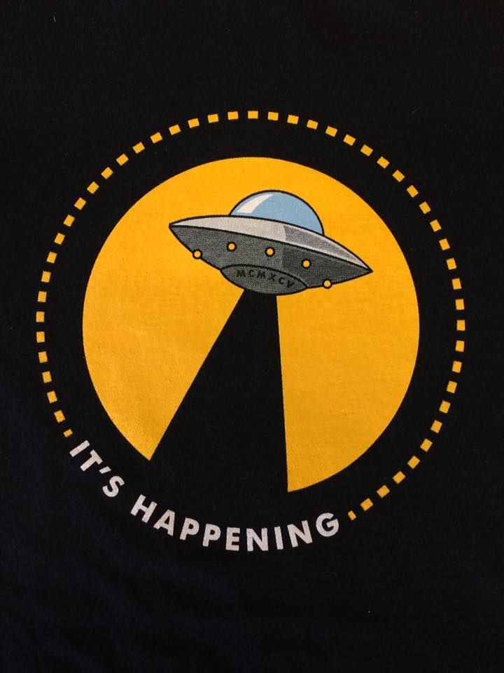 Black shirt design: UFO beaming down light over yellow circle with 