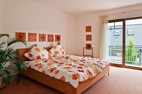 Bright bedroom with orange floral bedding, potted plant, and a balcony door letting in daylight