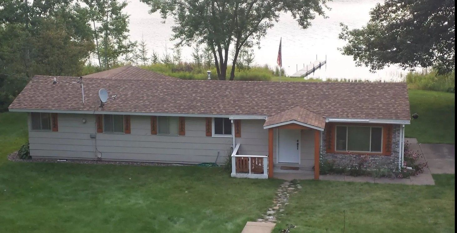 Single-story suburban house with a brown roof, white siding, and a small front porch surrounded by lawn.