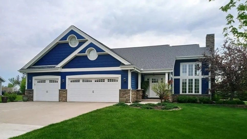 Blue suburban house with white trim, three-car garage, and a green lawn