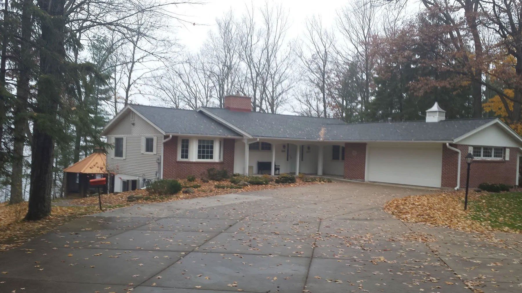 Single-story suburban house with a large driveway, leafless trees, and overcast autumn surroundings