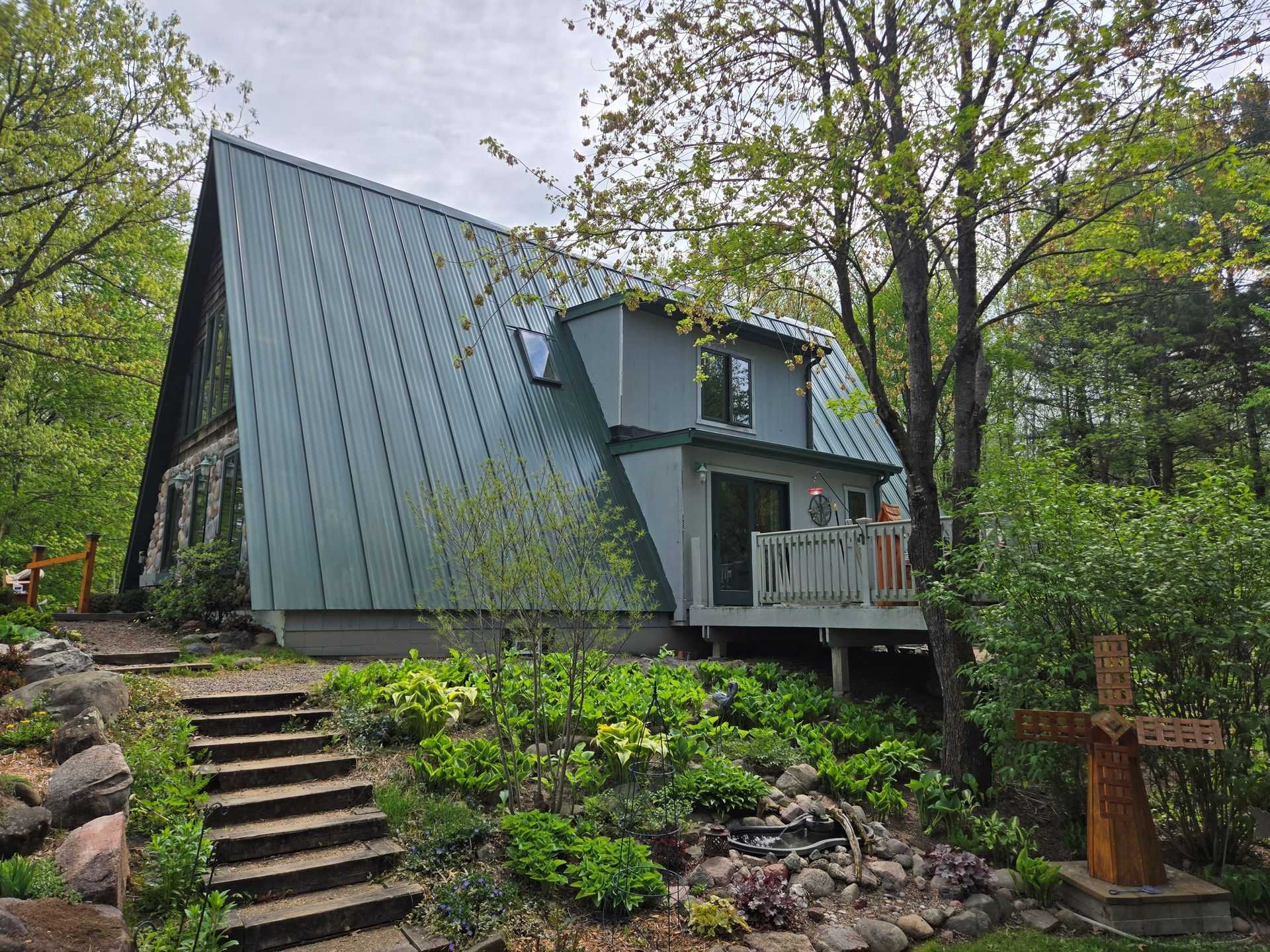 Modern gray cabin with steep metal roof nestled in a wooded garden, reached by stone steps