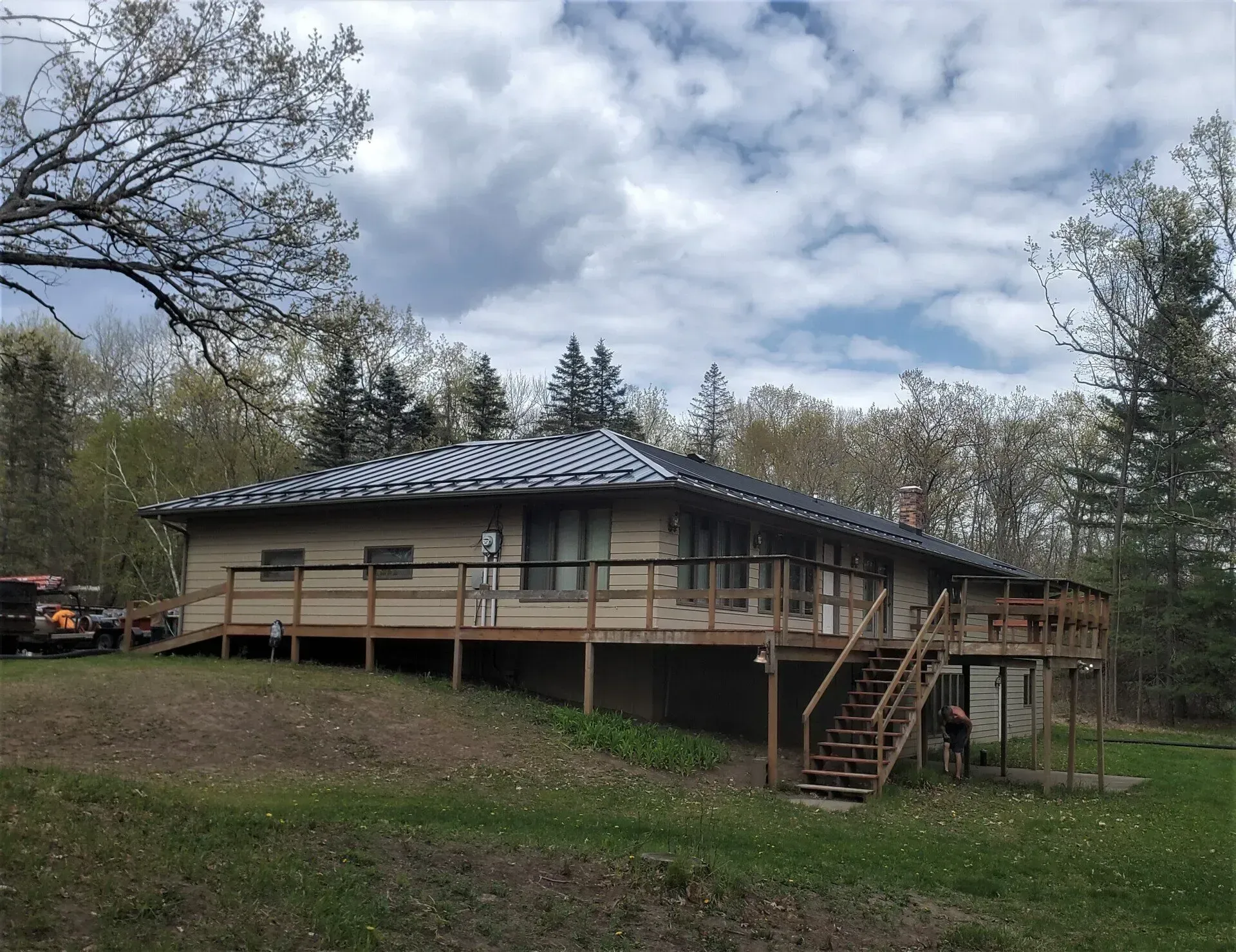 Single-story house with a raised deck and stairs, set in a grassy yard under cloudy skies.