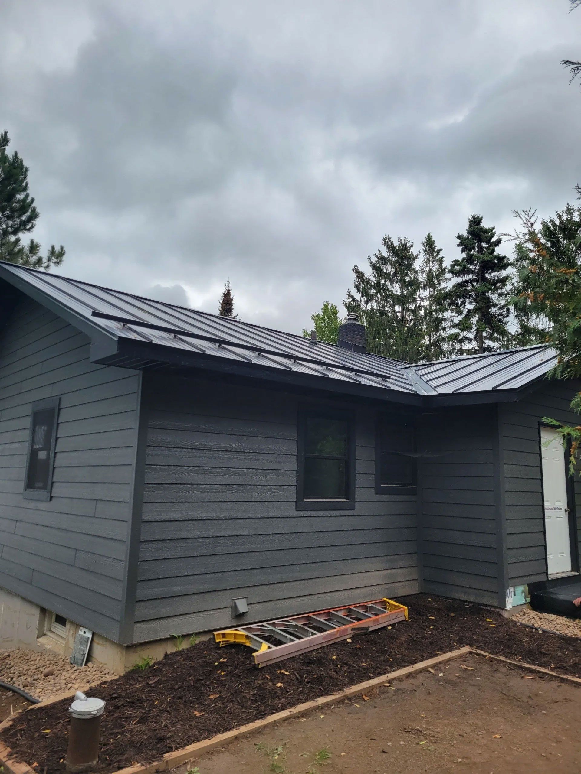 Gray house exterior with dark roof, small windows, and cloudy sky overhead