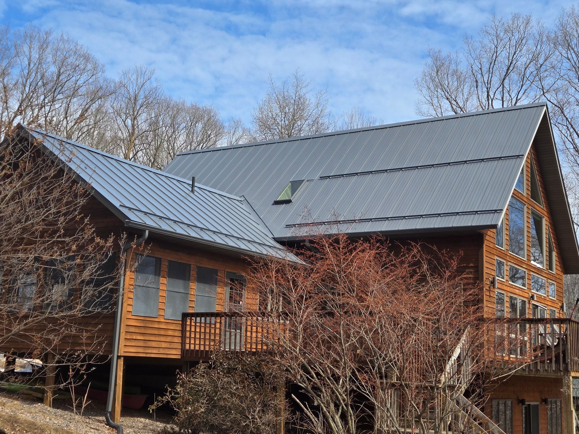 Wooden cabin with gray metal roof and leafless trees in a wooded setting