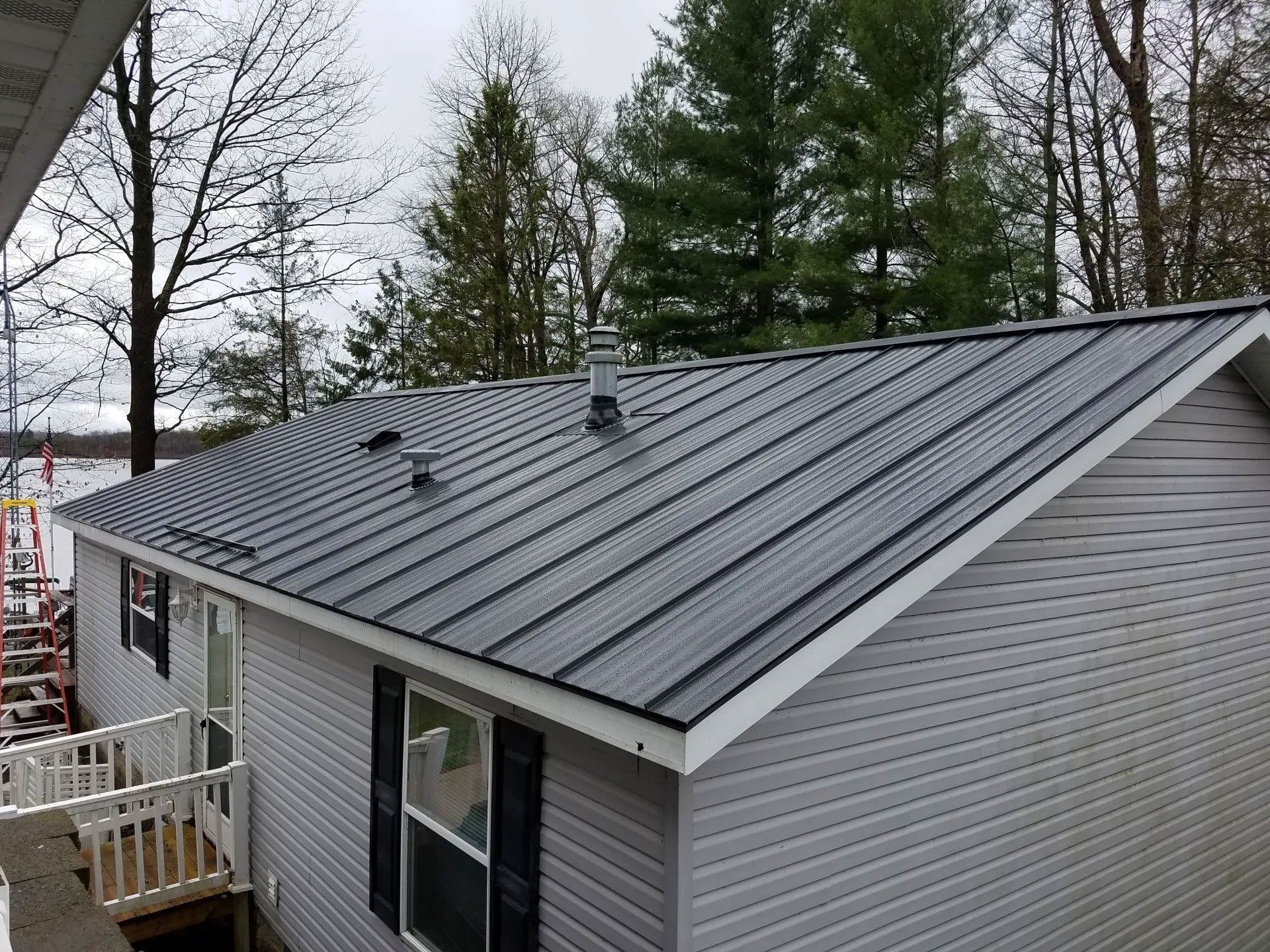 Gray metal roof on a house with trees in the background and a small deck in the foreground