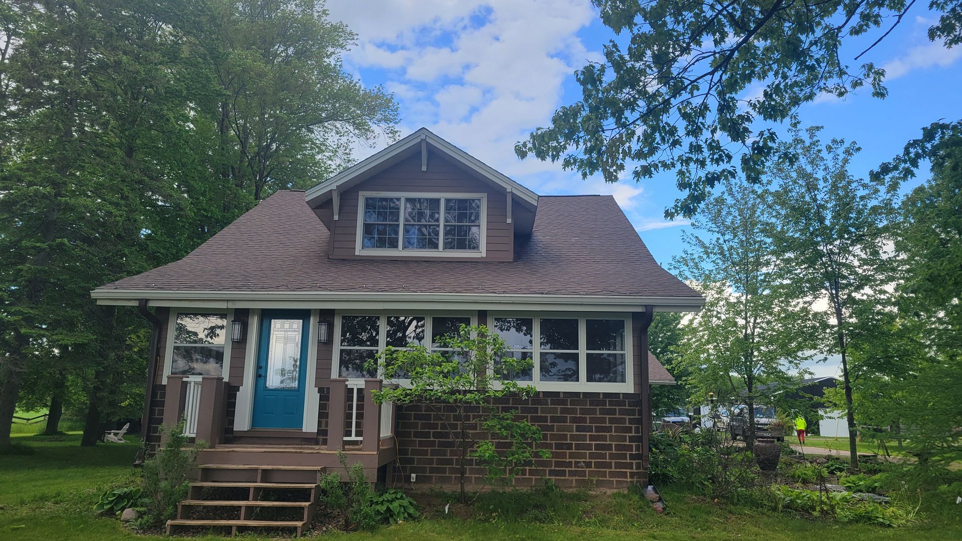 Small brick house with blue front door, gabled roof, and trees around it under a cloudy sky