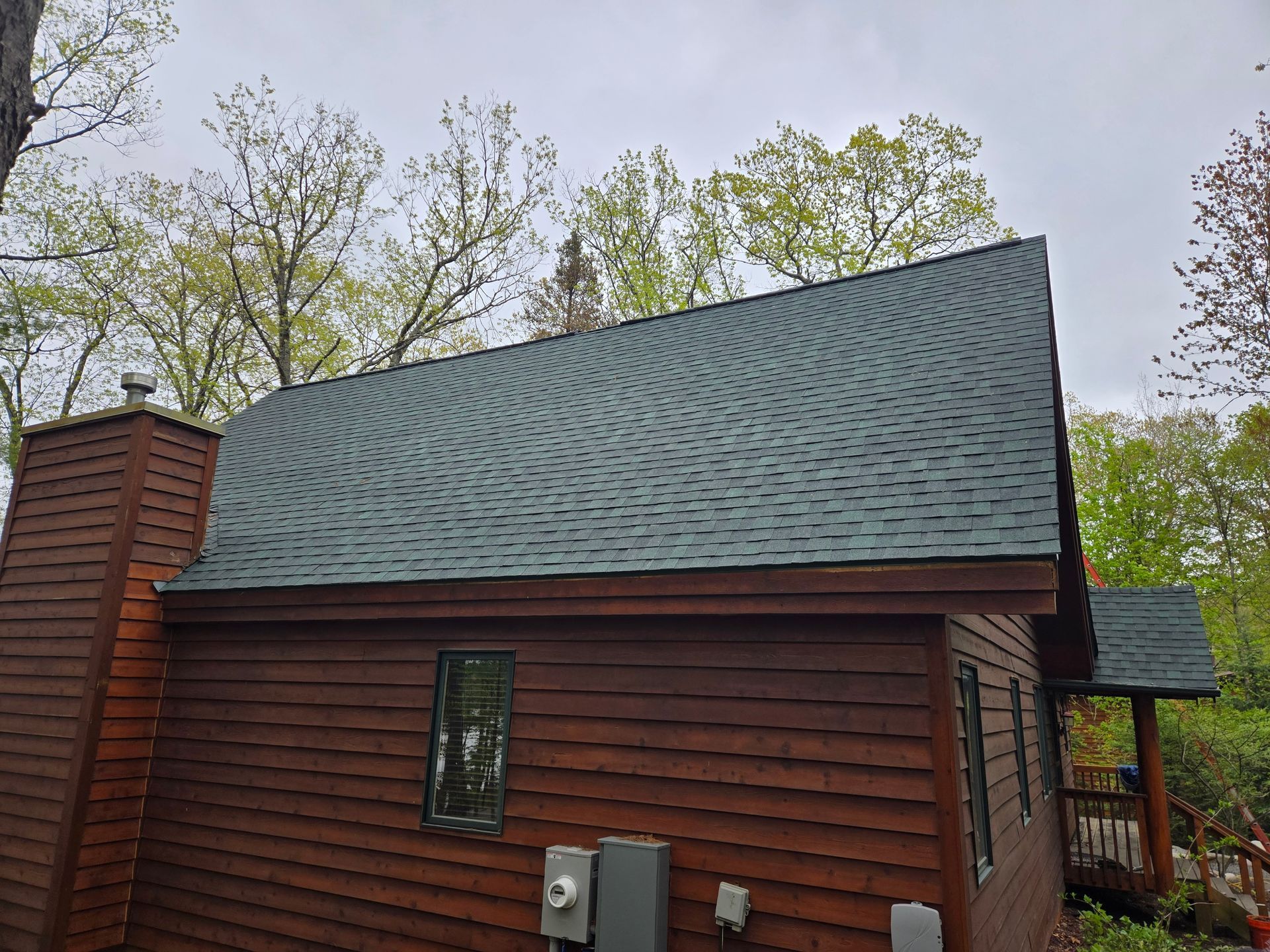 Wooden cabin with steep green roof and small windows amid trees under an overcast sky
