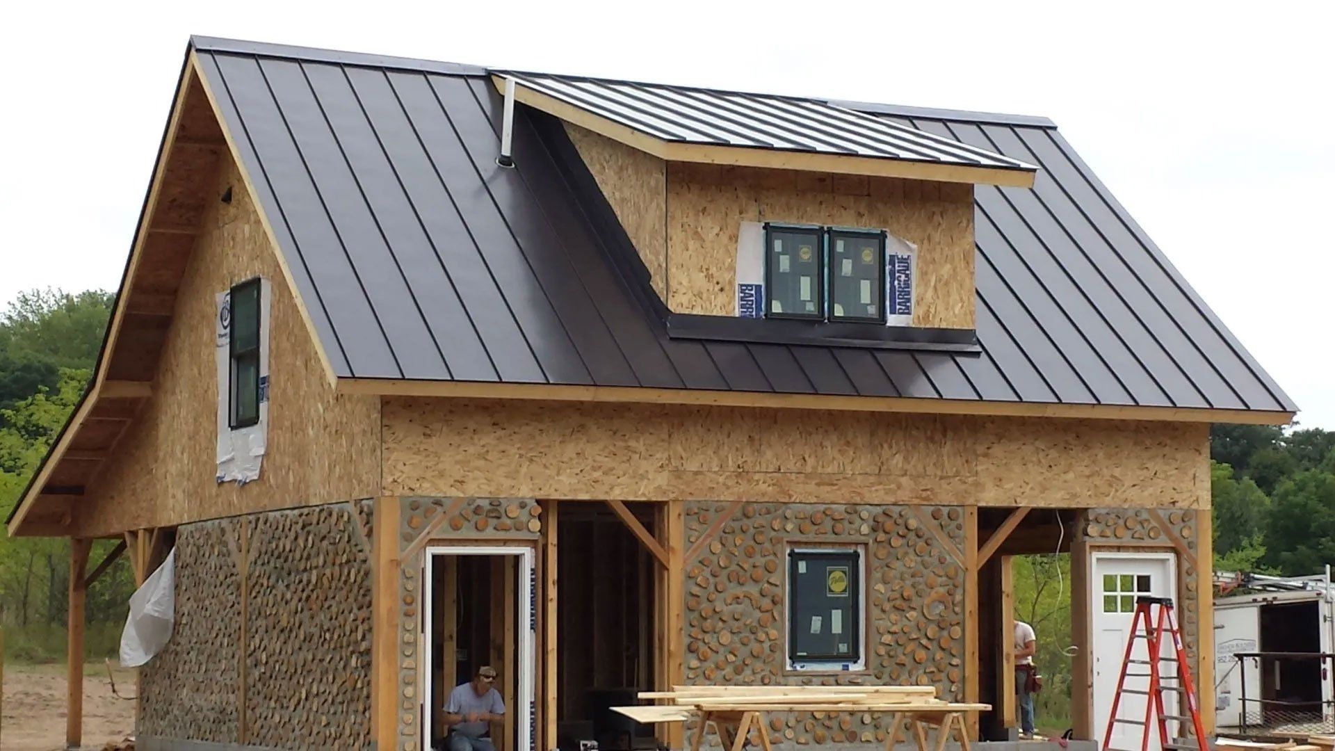 Partly finished two-story house with metal roof, exposed OSB walls, and ladders at the front
